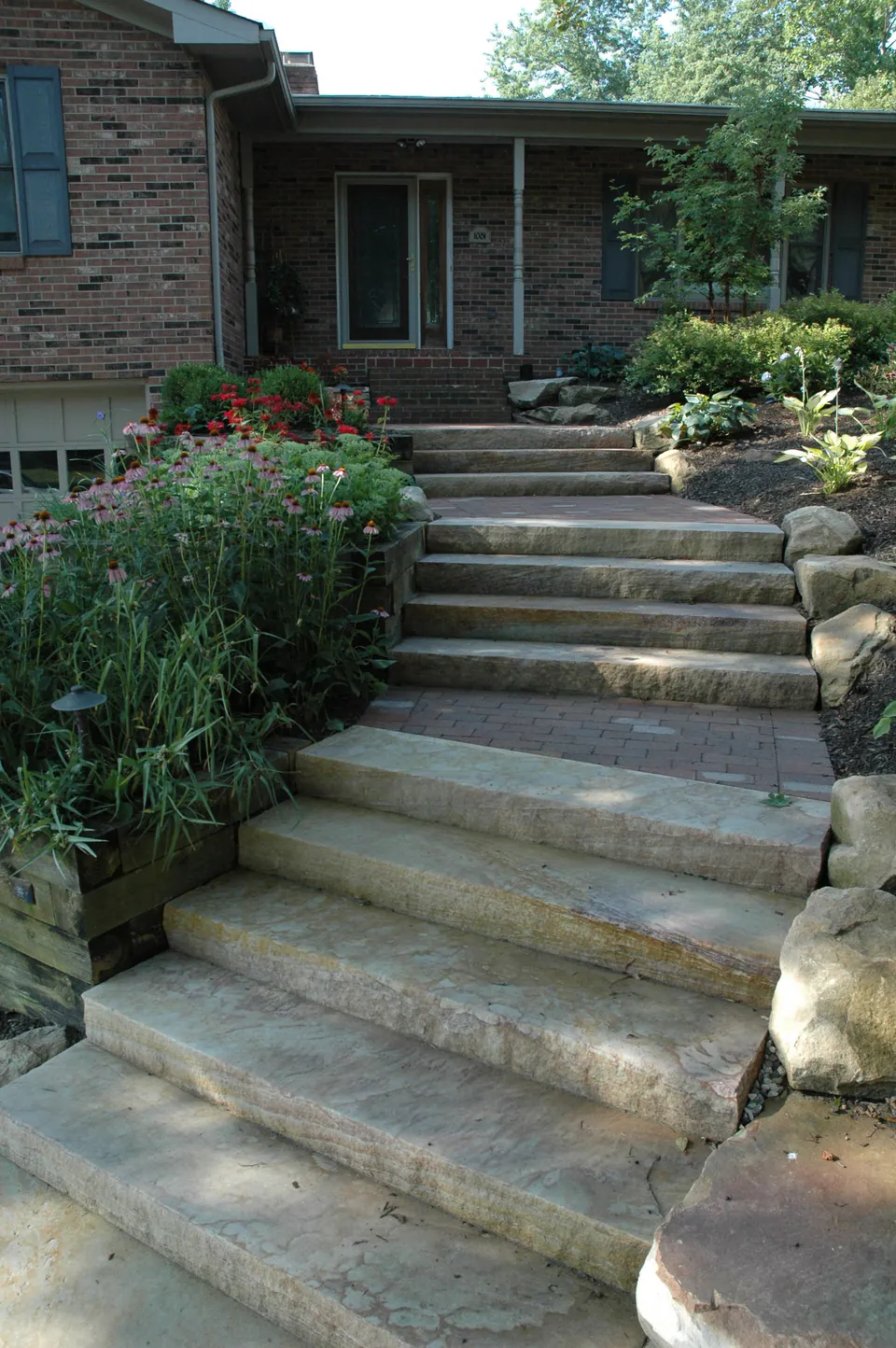 Series of wide stone slab steps down a front walk with boulders and planting on each side